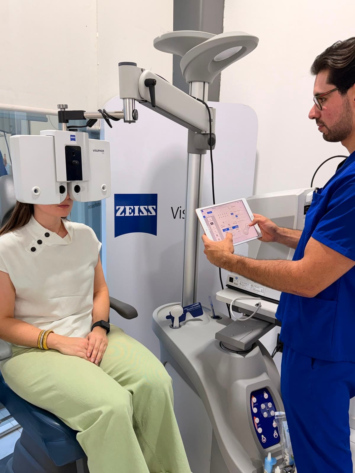 Optometrista realizando examen optométrico computarizado con equipo digital Zeiss y tablet.